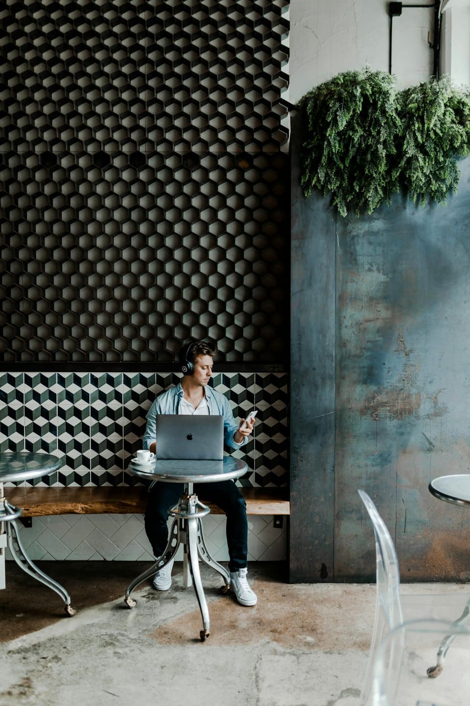 Man working on laptop and phone in a modern cafe.